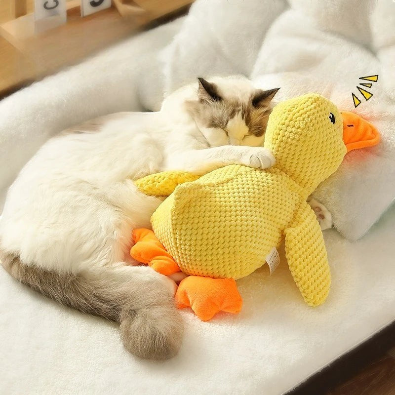 Valley of the Wolves Enten-Hundespielzeug aus gelbem Fleece, das von einer Katze als weiches Kuschelkissen genutzt wird